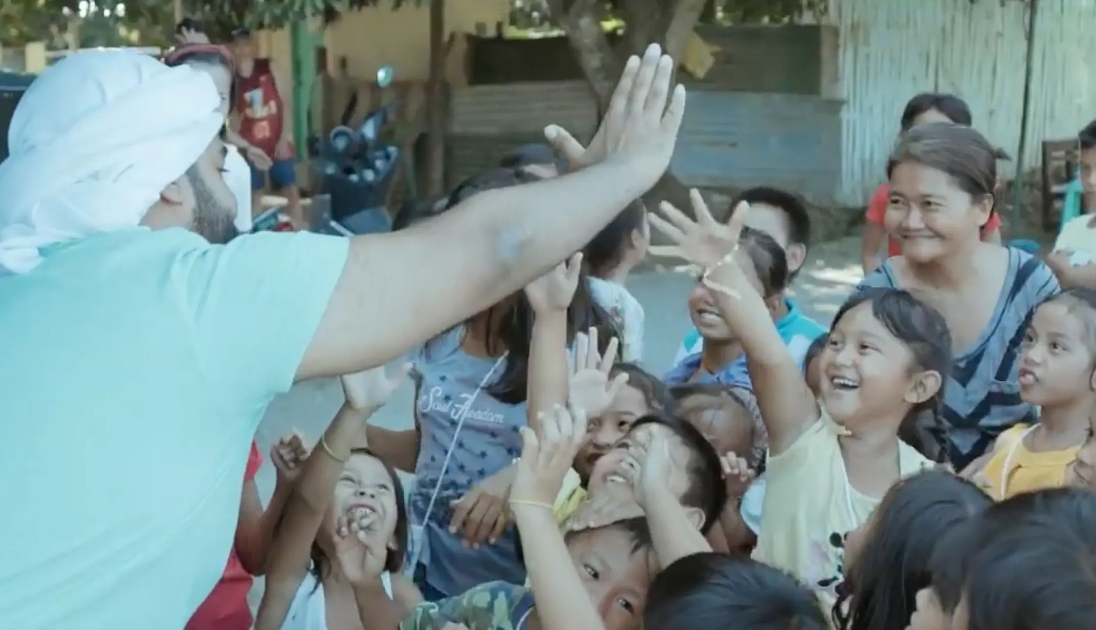 Children reaching up to high-five a man in a white ghutra during a community visit