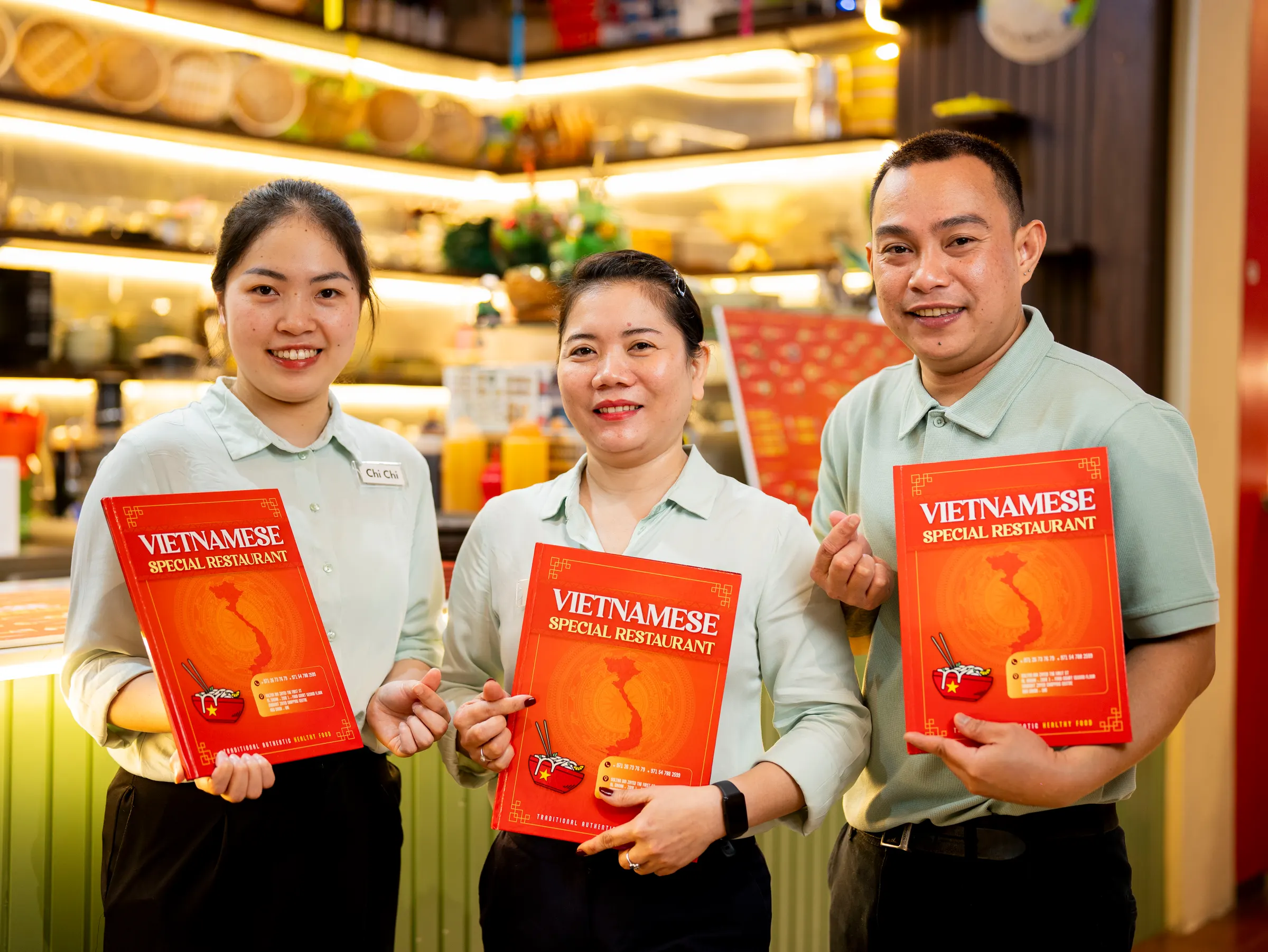 Three restaurant staff members holding menus in a brightly lit dining room